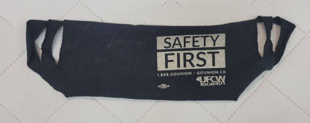 A black cloth mask printed with text reading, “Safety First. 1-888-GoUnion. GoUnion.ca. UFCW local 401.”