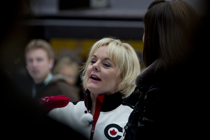 A blonde woman wearing a white jacket, among a crowd.