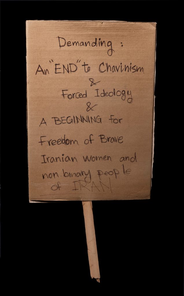 A protest sign reading “Demanding: An ‘END’ to Chavinism and Forced Ideology and a Beginning for Freedom of Brave Iranian women and non-binary people of Iran.”