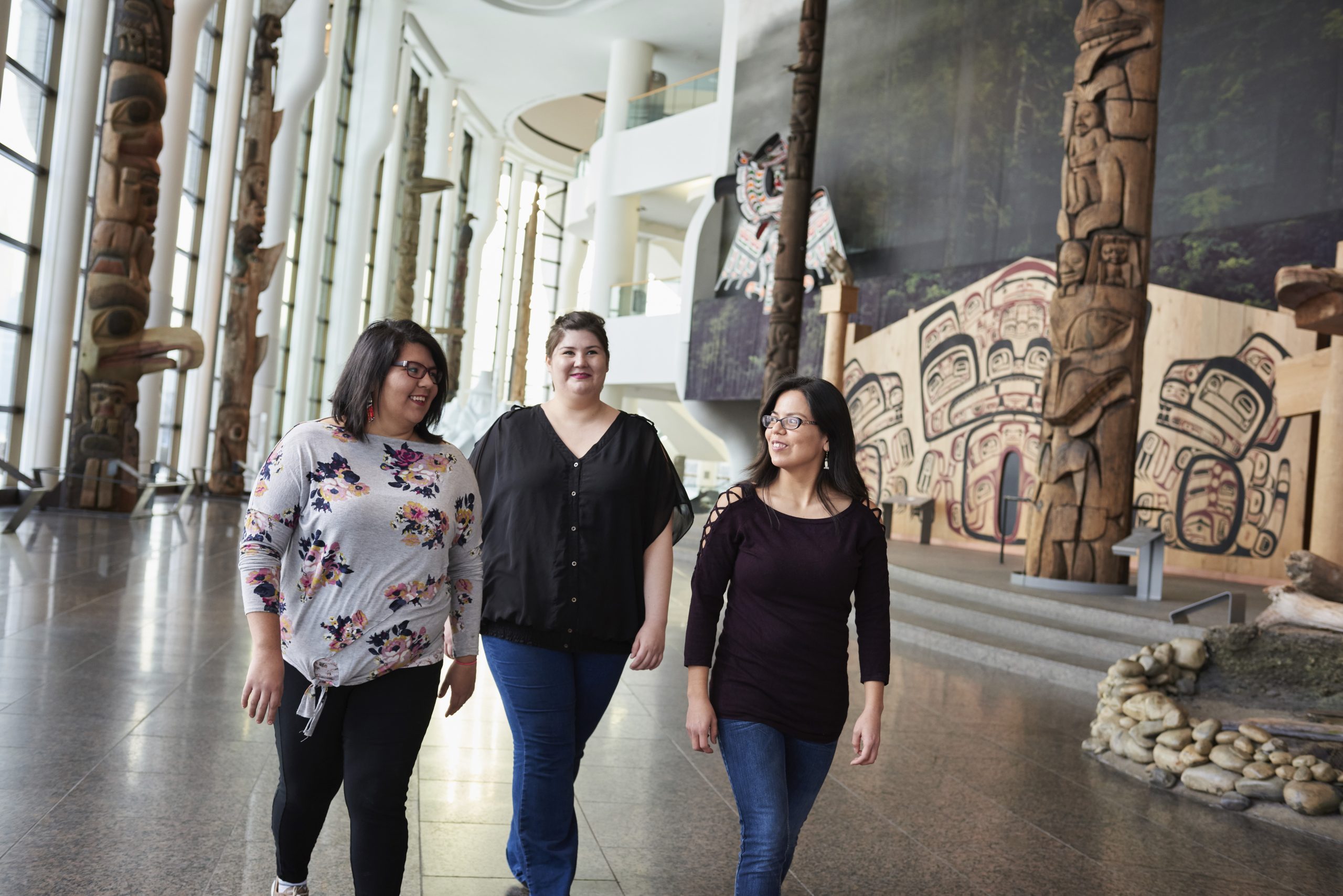 Three women walking through the Canadian Museum of History in Ottawa, admiring totem poles.