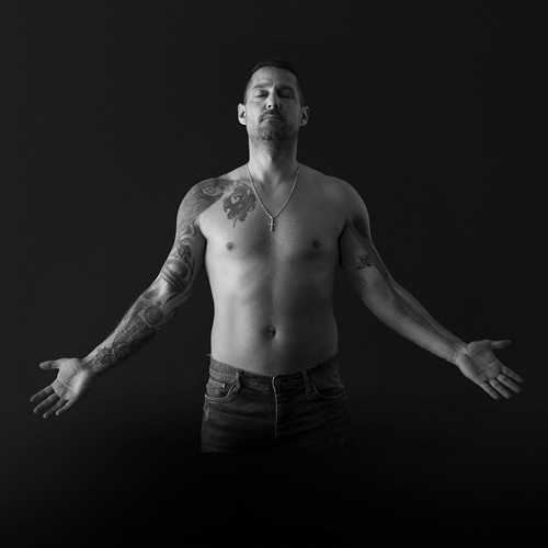 A black and white photo of a shirtless man with tattoos.