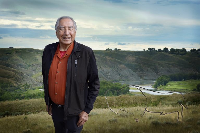 Dr. Little Bear smiles, standing in front of a rolling green landscape.