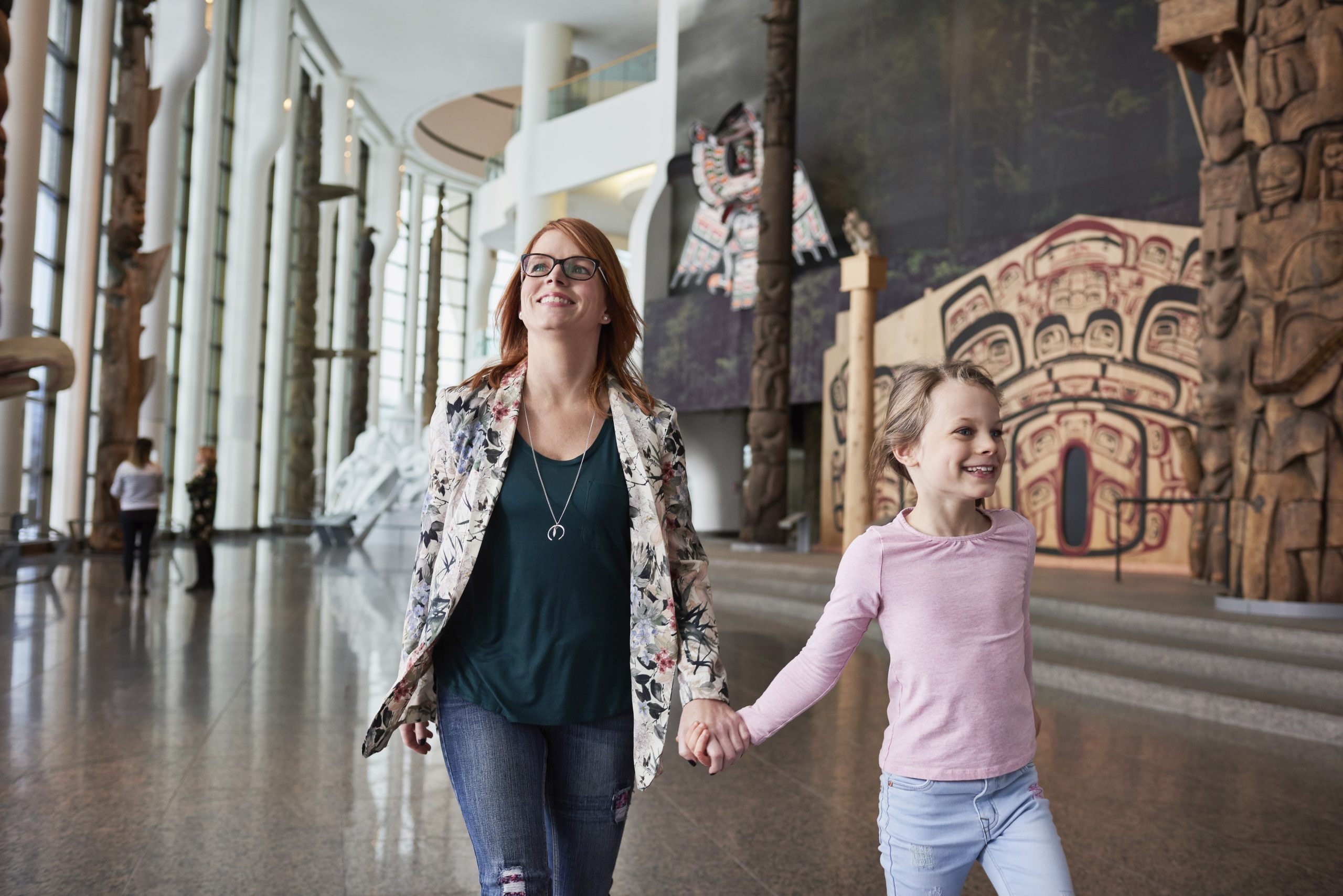 A woman and a child walk hand in hand through the Canadian Museum of History in Ottawa, surrounded by various artworks and exhibits on display.