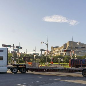 Large truck in front of a sandstone-coloured Museum building, with the Monument lying on a long trailer.