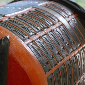 A view of the lower body of the Monument, lying on its side. The large cylindrical shape is covered with carved faces set within a bright orange grid.