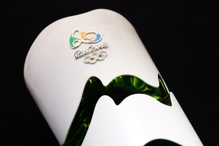 Close up of the end of a white Olympic torch with dark green curved lines and the Rio 2016 logo.