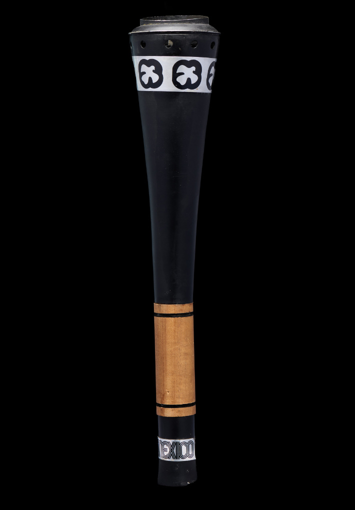 Black Olympic torch with white accented designs and wood where the torch is held.