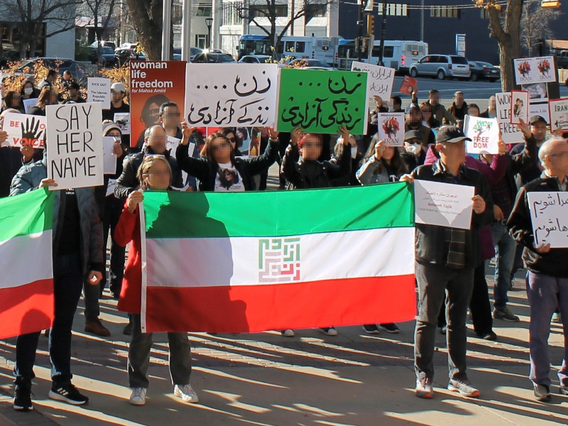 A crowd of people carrying placards and Iranian flags.