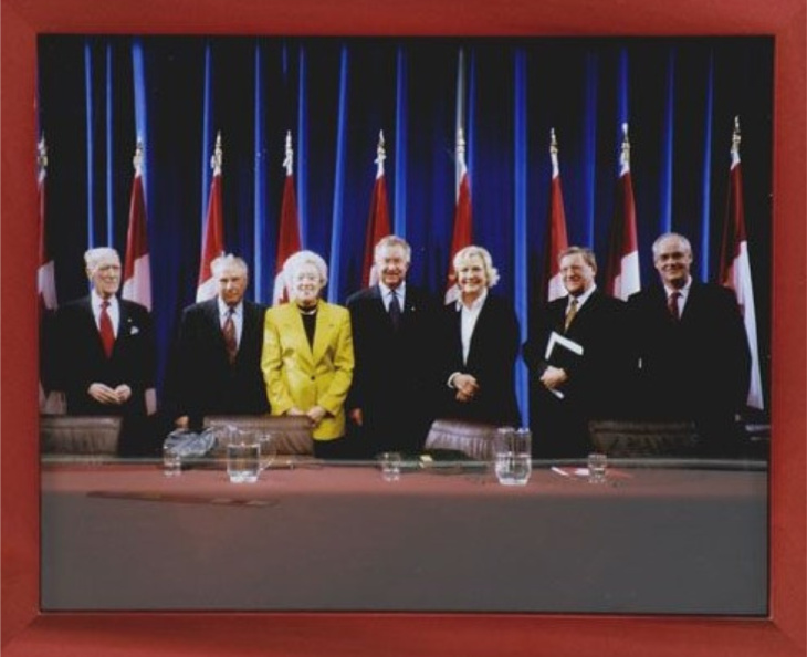 Photograph of 5 men and 3 women dressed in suits and business attire standing behind a table with Canada flags behind them.