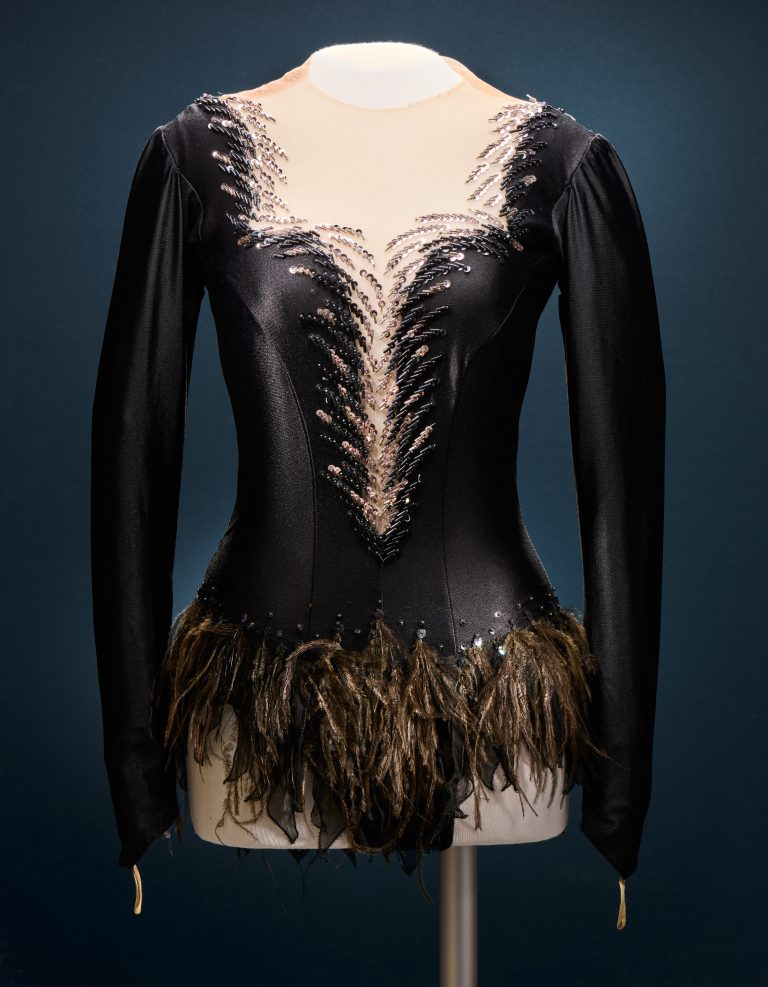 A tight black skating dress made of a shiny material, with a plunging neckline and trimmed with crystals and feathers.