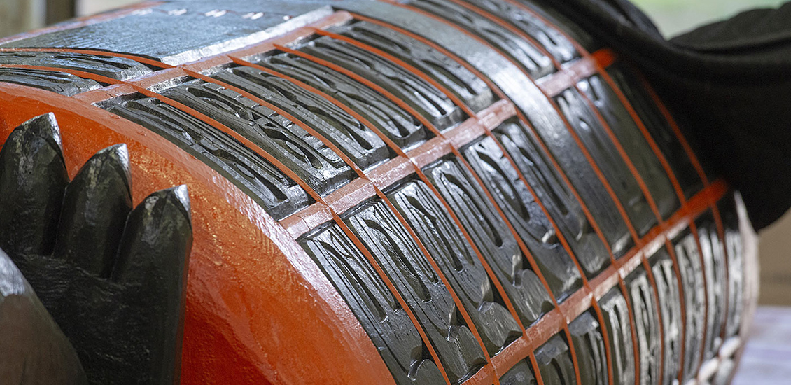 A view of the lower body of the Monument, lying on its side. The large cylindrical shape is covered with carved faces set within a bright orange grid.