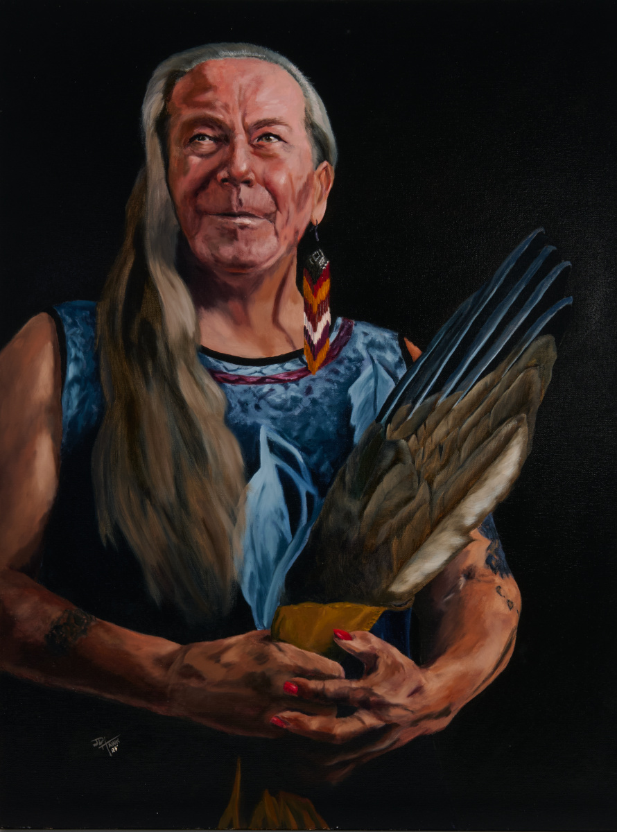 A waist-up painted portrait of Charlotte Nolin posing off-centre to the left against a dark black background. She has long greying hair cascading down the right side of her chest, and her exposed left ear is adorned with a dangling beaded earring. She has a warm, strong, almost-smiling expression and is looking above and to the left of the viewer. Around waist level, her left hand — with painted-red nails — cradles her right hand, which holds a narrow fan of eagle feathers bound with leather that extends diagonally past her left shoulder.