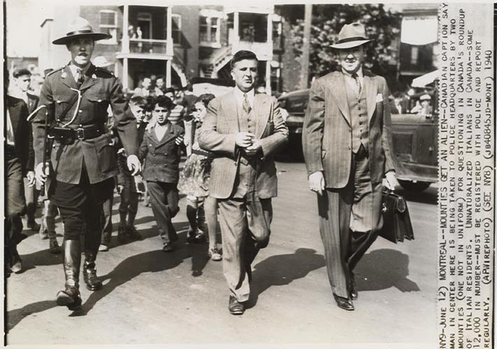 A man in a suit is accompanied by an RCMP officer and another man in a suit and hat, carrying a briefcase.