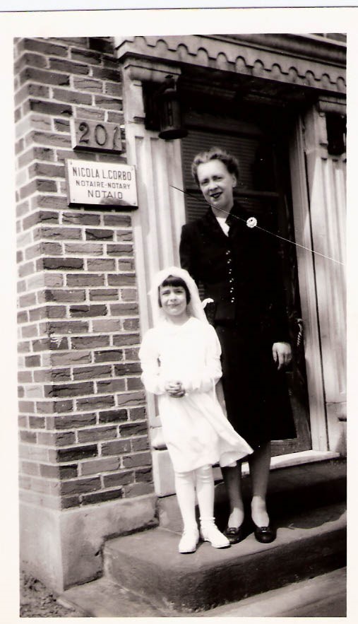 Black-and-white photograph of a young girl in a white dress, with a woman standing behind her.
