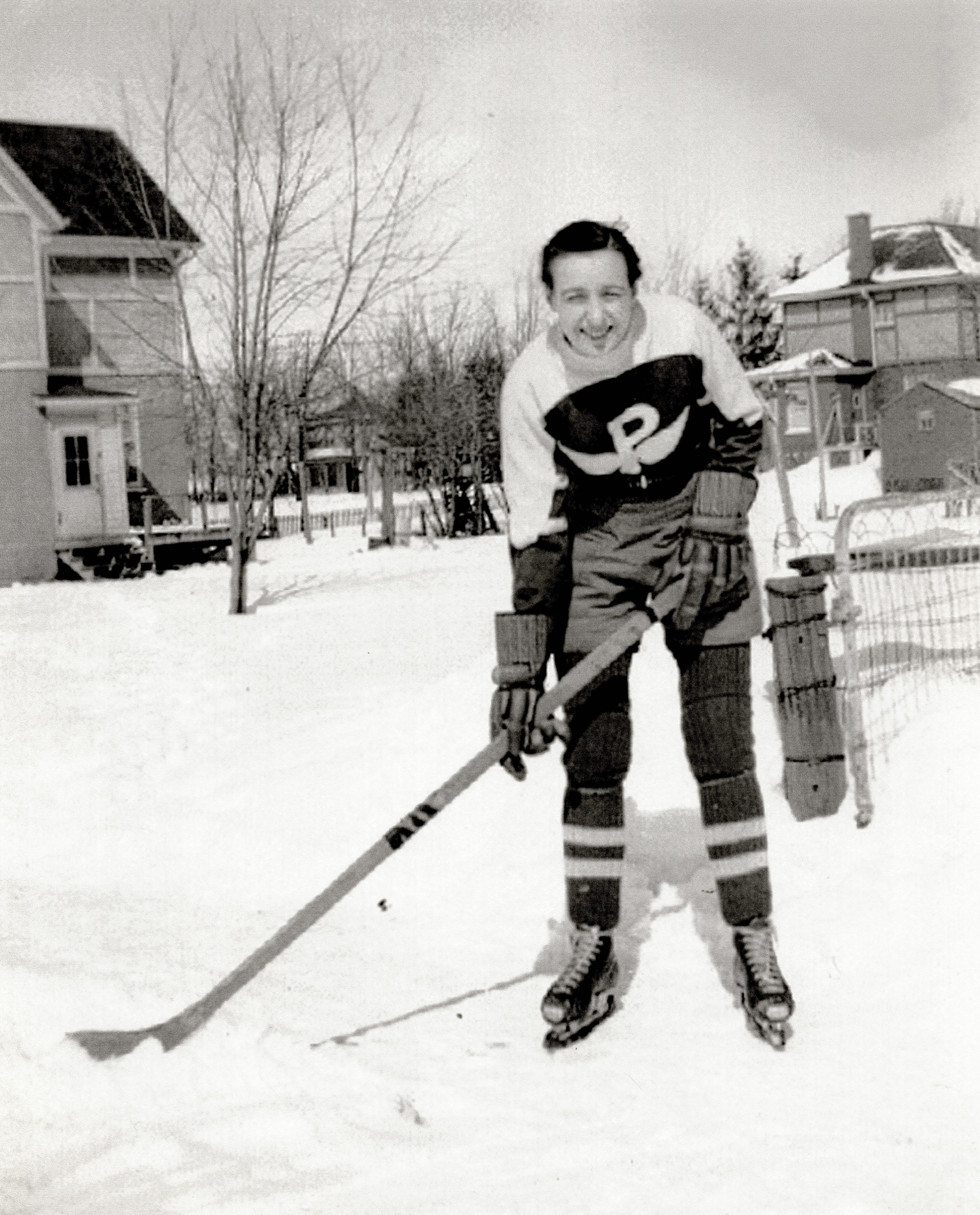 Black and white photo of a woman wearing hockey equipment on a backyard rink